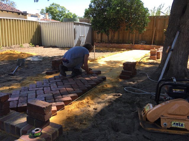landscaper laying brick pathway in garden